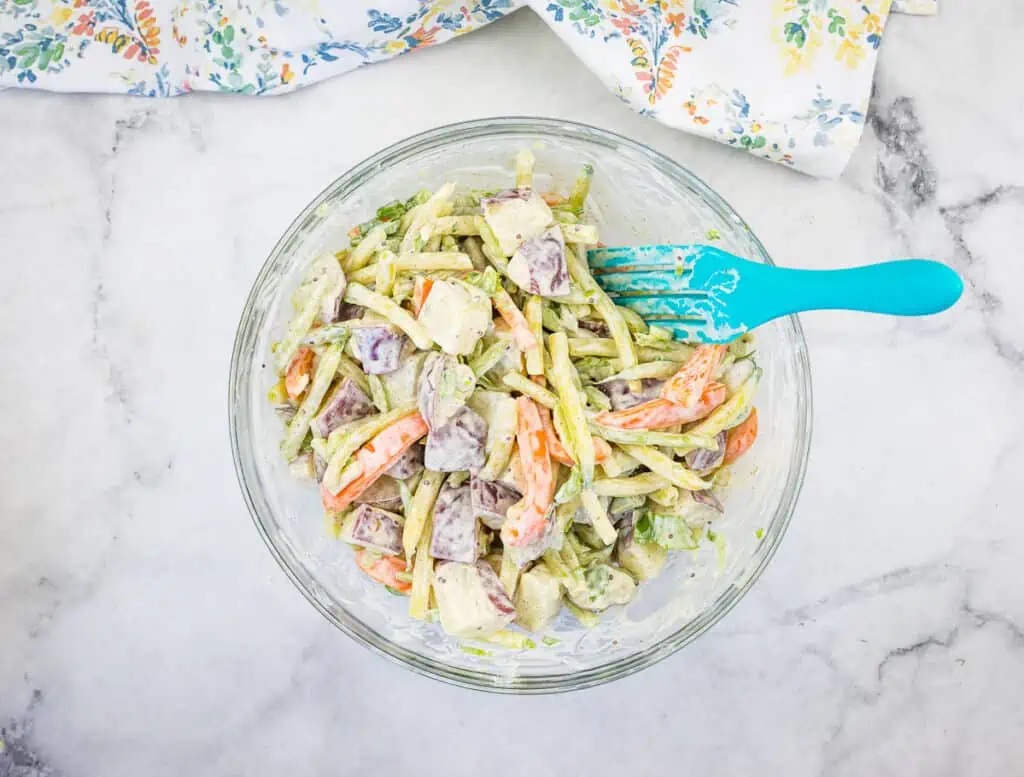 A bowl of Yellow Bean & Potato Salad with a blue spatula.