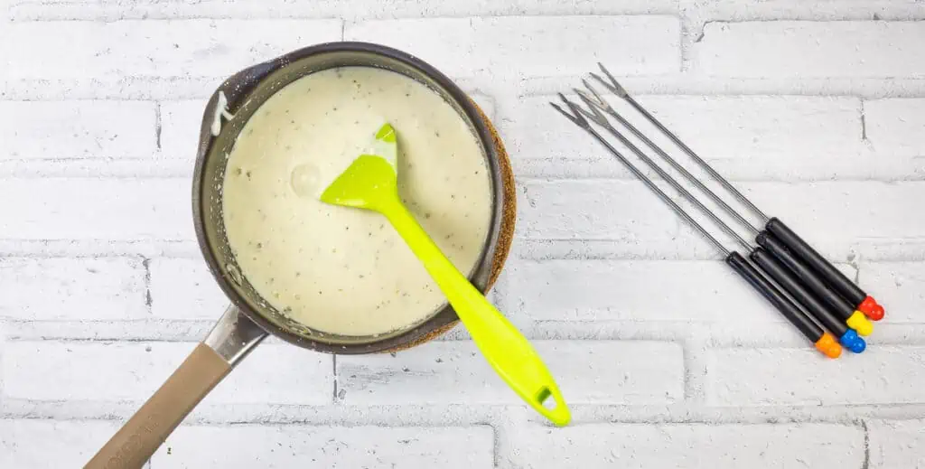 A frying pan with cheese sauce and a pair of spatulas.