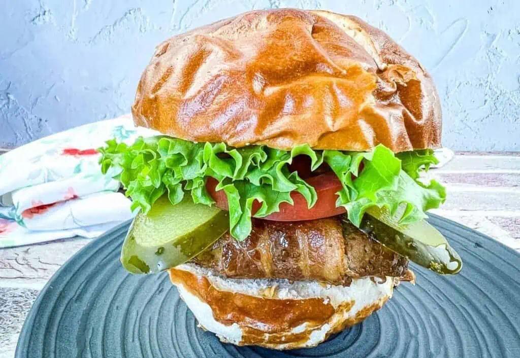 A burger with lettuce, tomatoes and pickles on a plate.