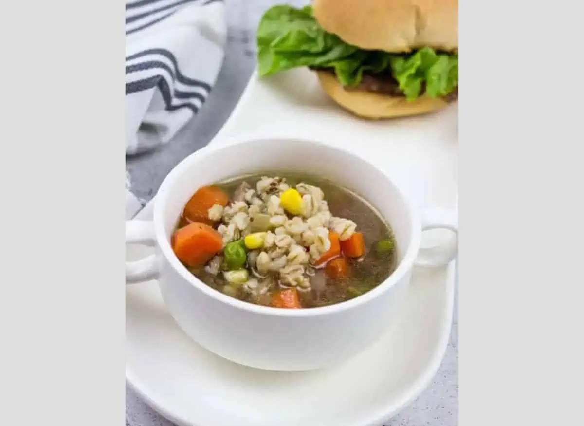 A bowl of Beef and Barley Soup with a burger on a long white tray.