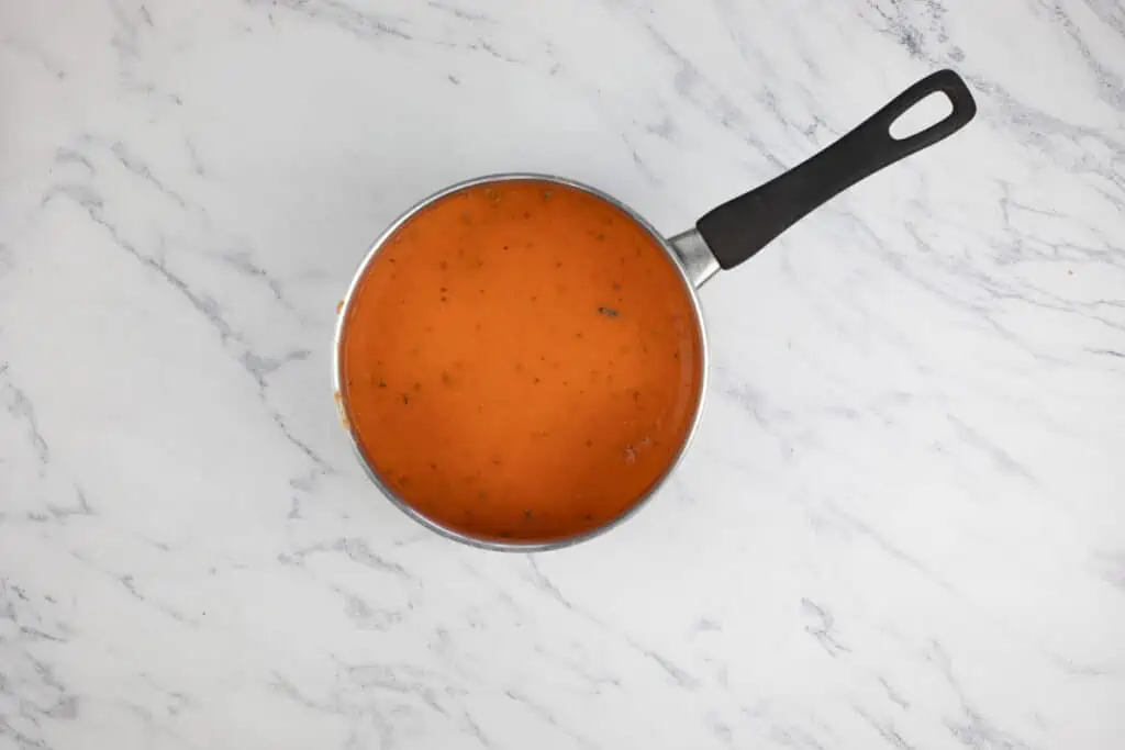 Red pepper and tomato soup in a pan on a marble surface.