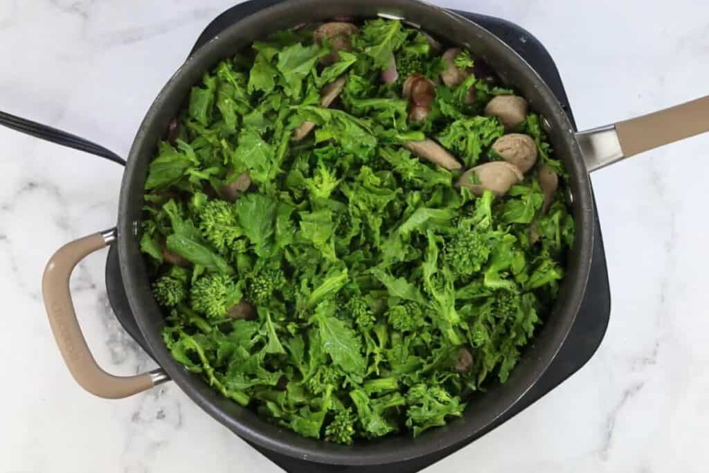 A pan with broccoli rabe and sausage in it.
