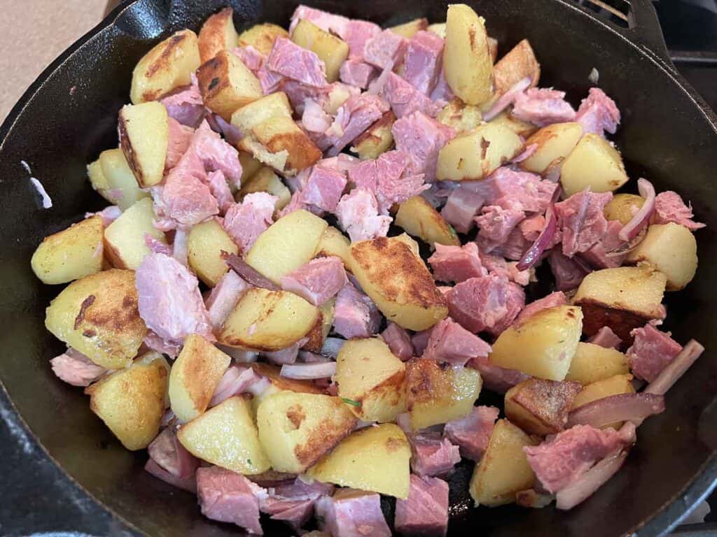 Ham and potatoes in a skillet on a stove.