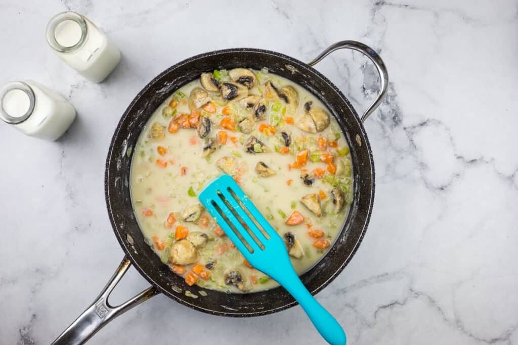 A skillet with mushrooms and milk in it.