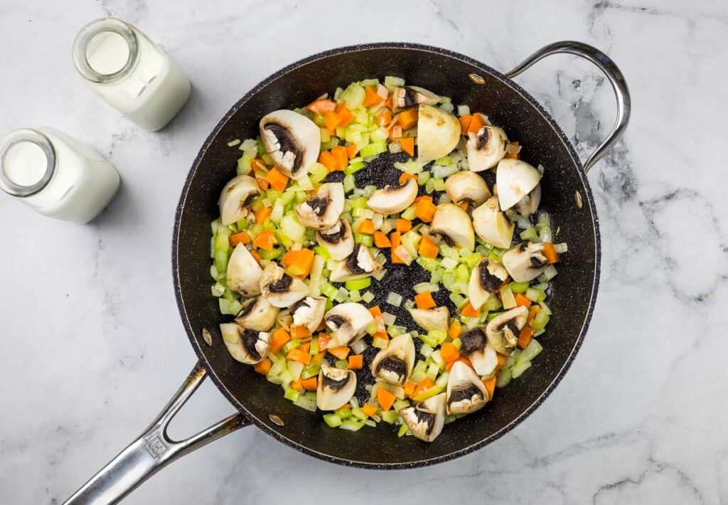 A frying pan full of vegetables and mushrooms.