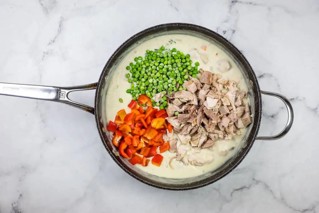 A pan with meat, vegetables and peas in it.