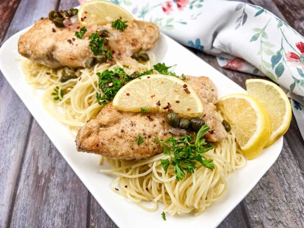 Chicken with lemon and capers on a white plate.