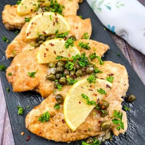 Chicken Picatta with lemon and parsley on a black plate.
