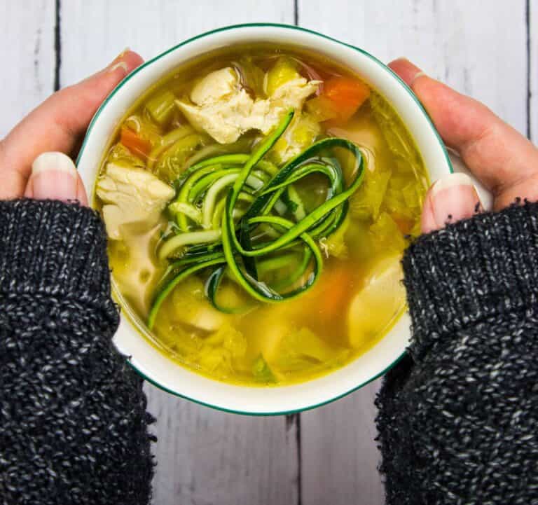 A person holding a bowl of chicken and zucchini soup.