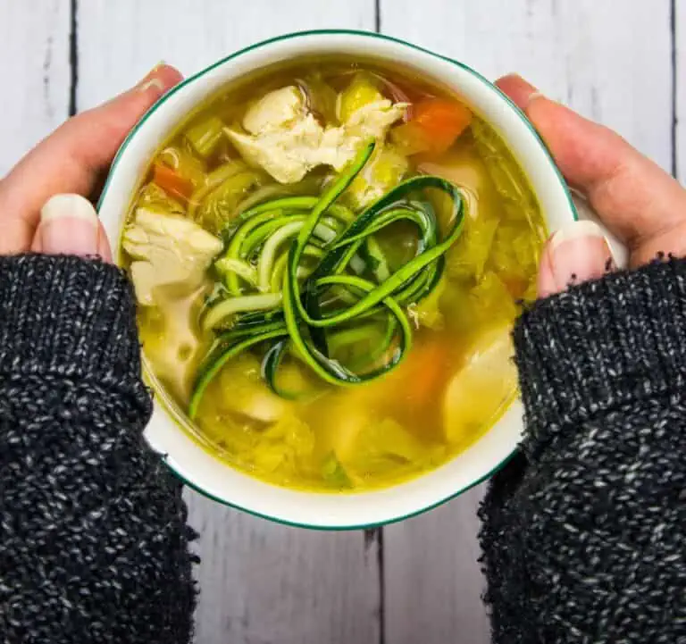 A person holding a bowl of chicken and zucchini soup.