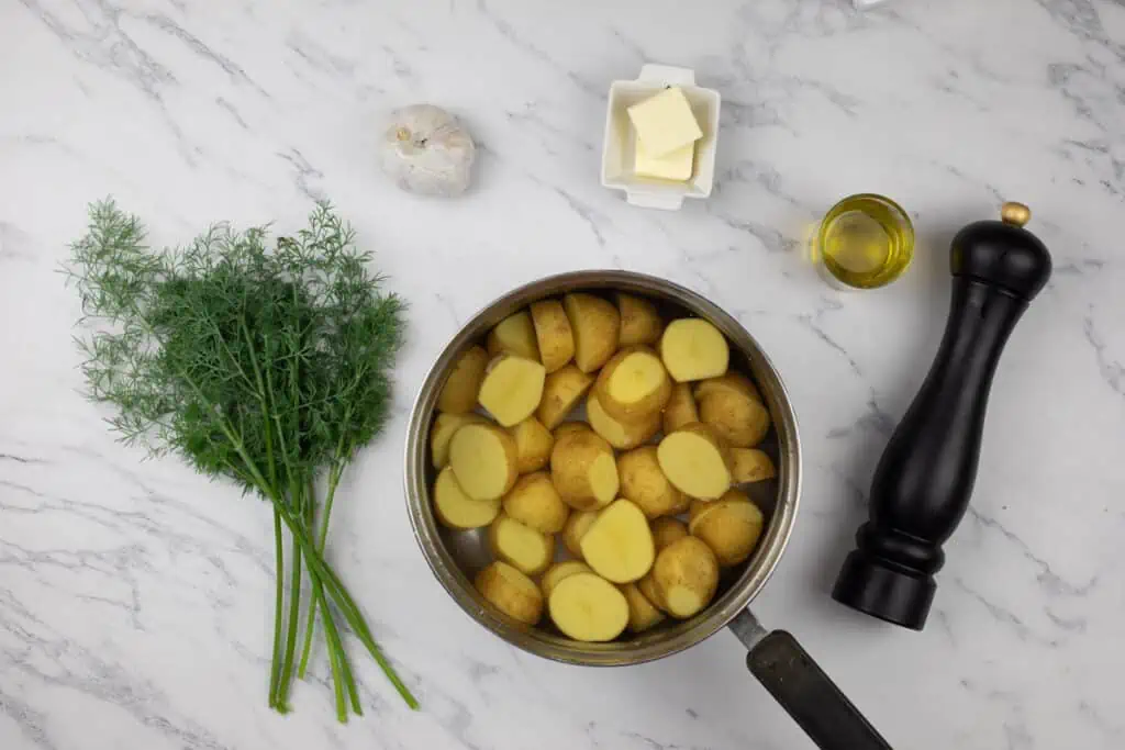 A pan with potatoes, butter and dill on a marble table.