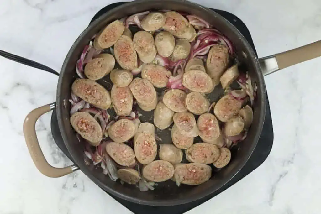 A pan with sausages and onions in it.