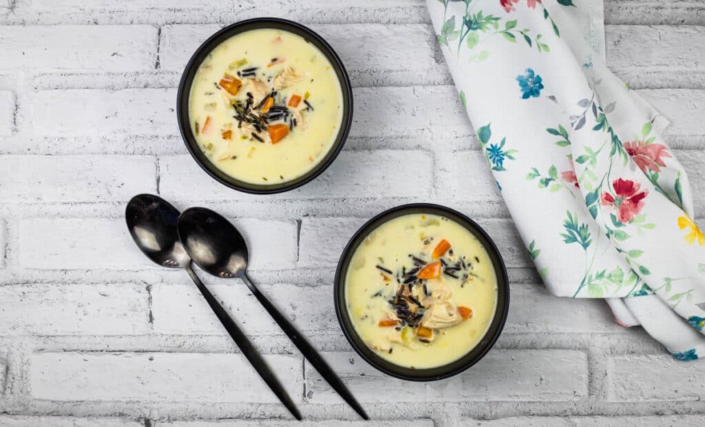 Two bowls of soup with spoons on a white brick wall.