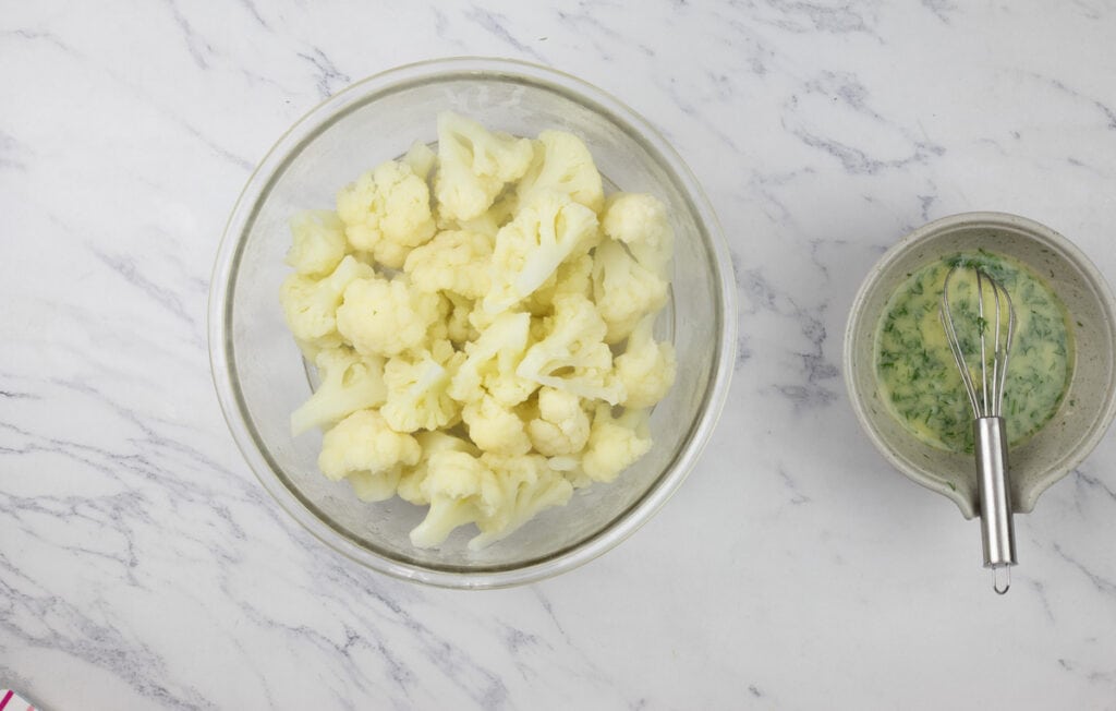 Cauliflower in a bowl next to a bowl of green sauce.