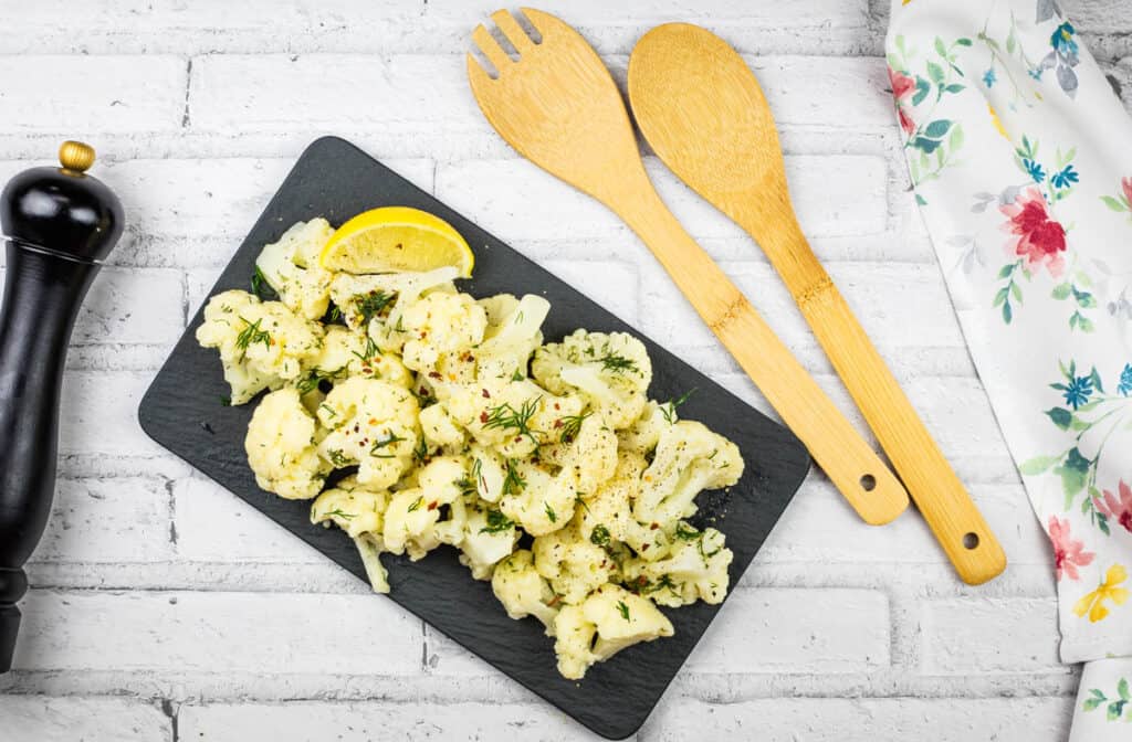 Roasted cauliflower with lemon and herbs on a black plate.