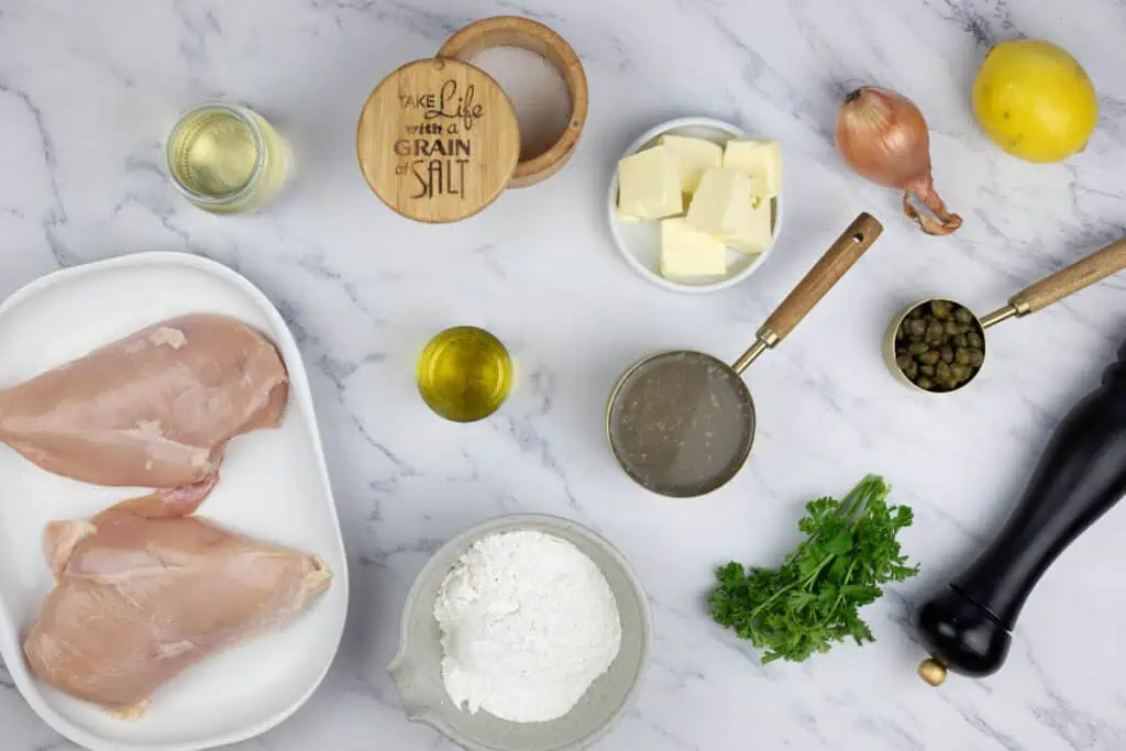 The ingredients for a chicken dish are laid out on a marble table.