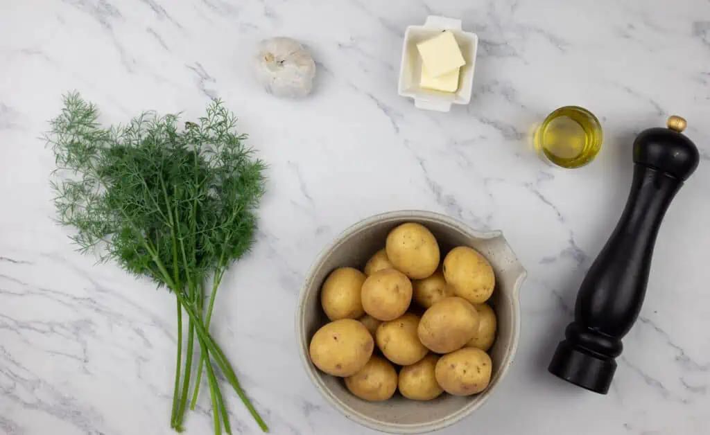 A bowl of potatoes, butter and dill on a marble table.