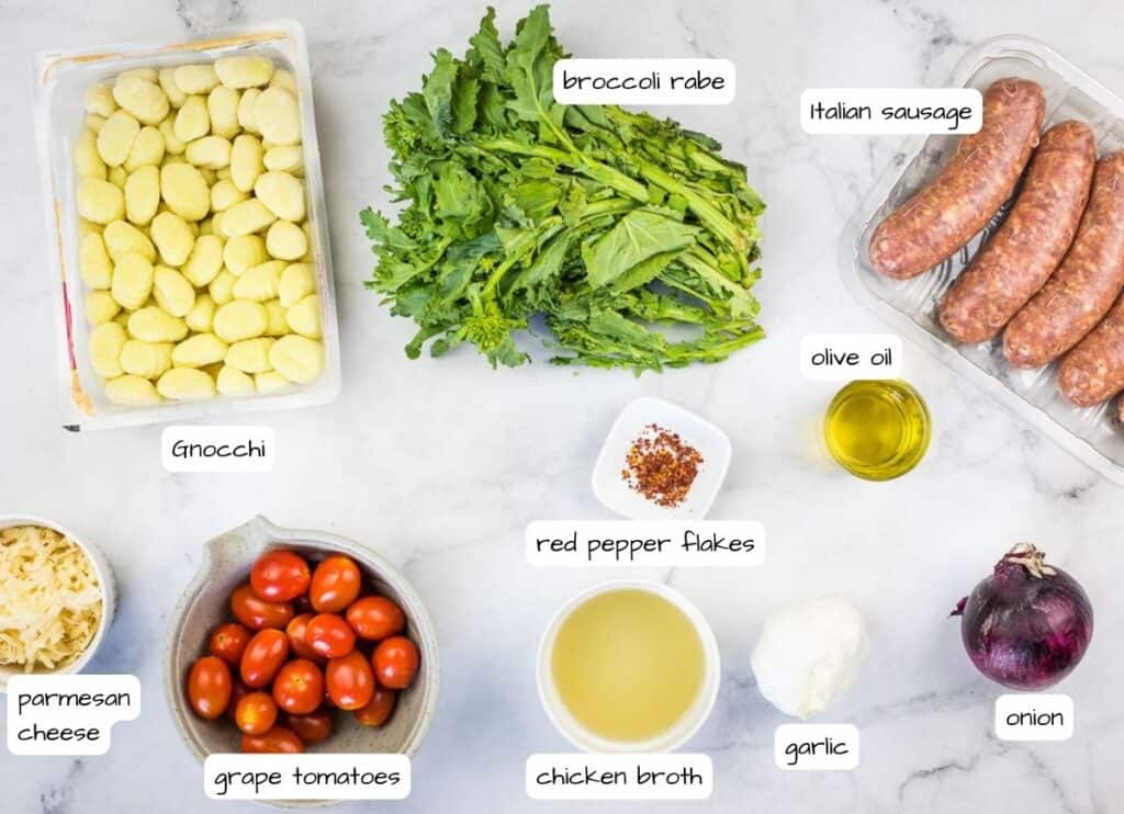 Ingredients for meatballs with sausage and tomatoes on a marble countertop.