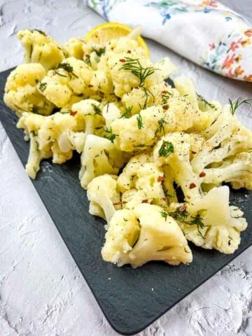 Cauliflower with lemon and dill on a black plate.