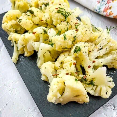 Cauliflower with lemon and dill on a black plate.