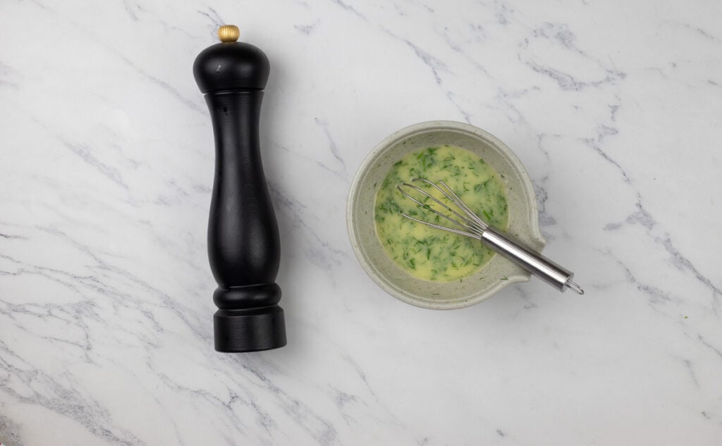 A black pepper grinder next to a bowl of green sauce.