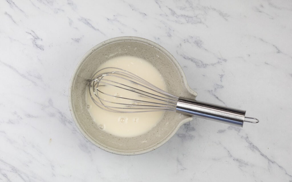 A bowl with a whisk in it on a marble surface.