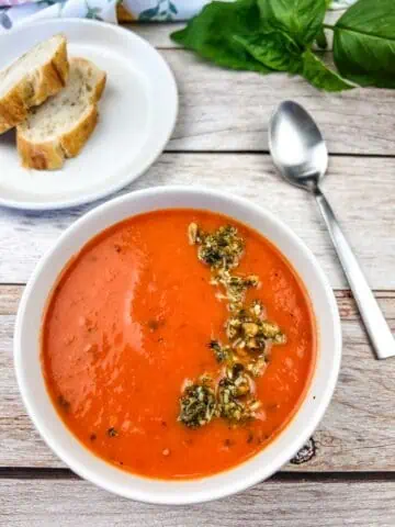 A bowl of tomato soup with bread and basil.
