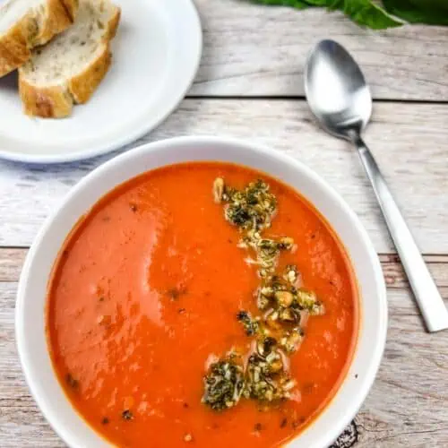 A bowl of tomato soup with bread and basil.