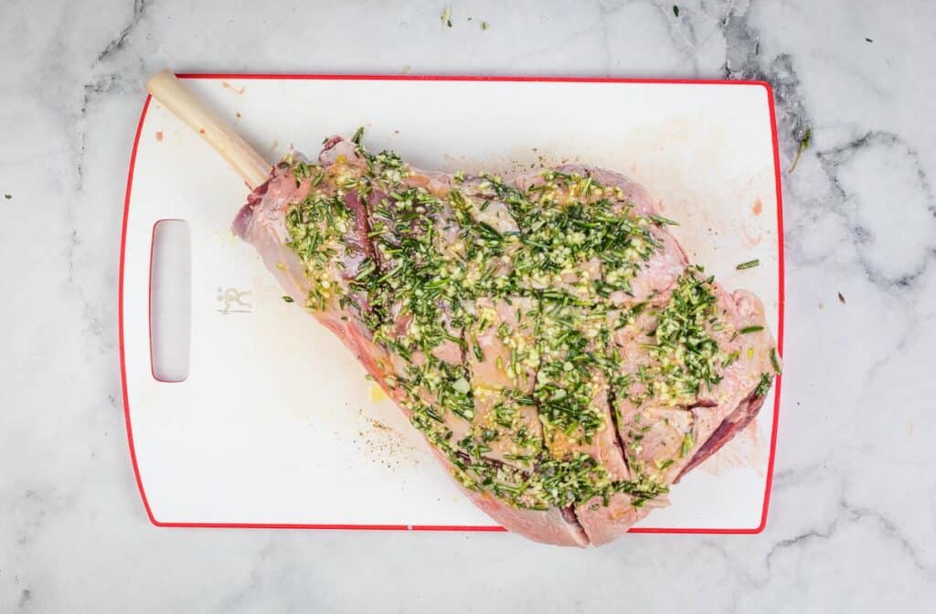 A piece of meat with herbs on a cutting board.