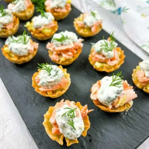 Smoked salmon tartlets with dill on a tray.