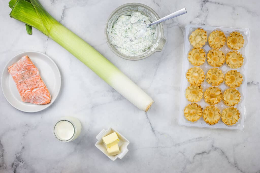 The ingredients for a salmon and leek tartare are laid out on a marble table.