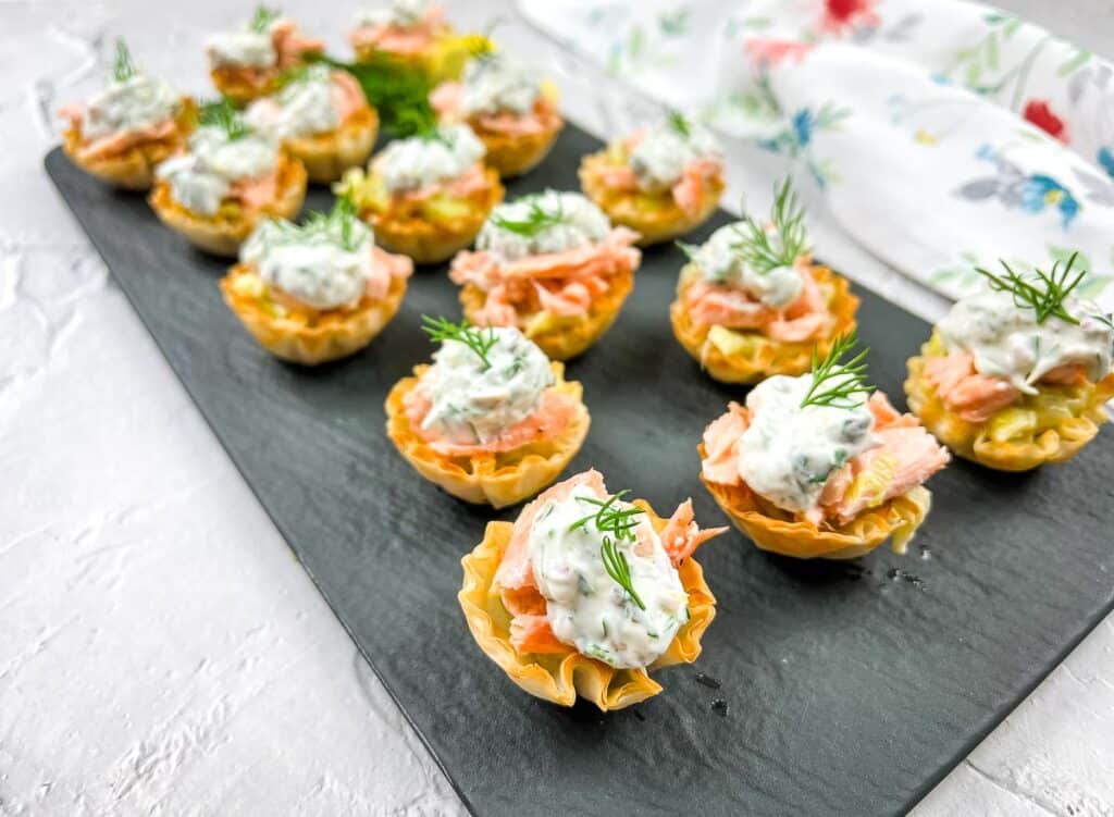 Smoked salmon tartlets with dill on a tray.