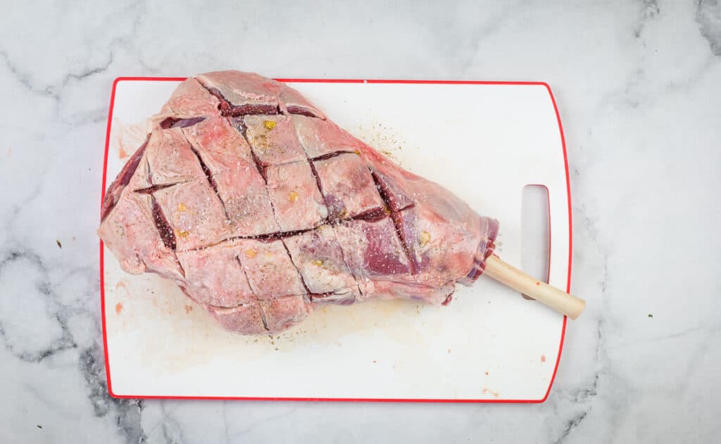 A scored leg of lamb on a cutting board.