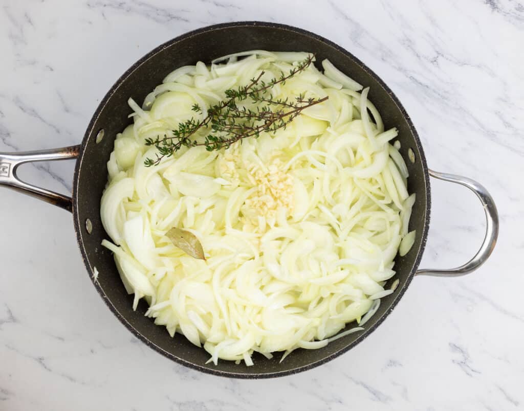 Onions in a pan with a sprig of thyme.