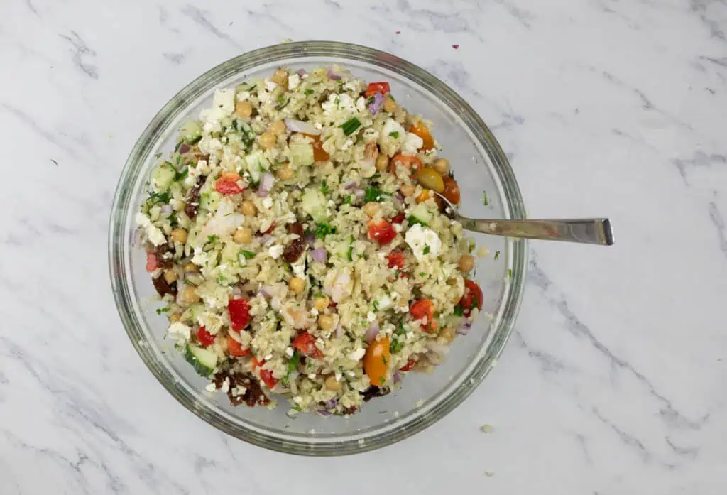 A bowl of greek couscous salad on a marble table.