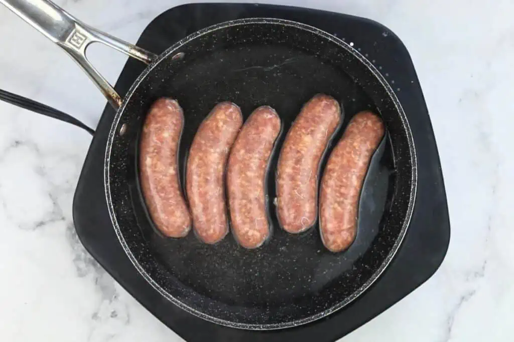 Sausages are being cooked in a frying pan.