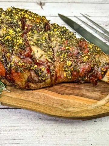 A roasted lamb on a wooden board with a knife and fork.