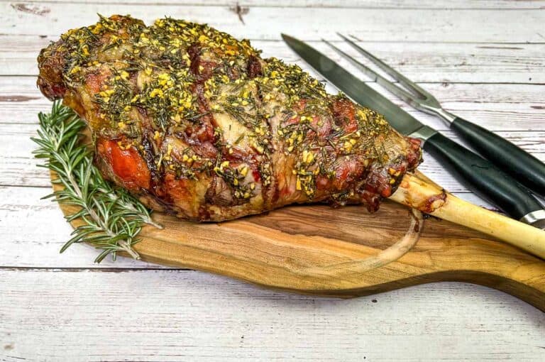 A roasted lamb on a wooden board with a knife and fork.
