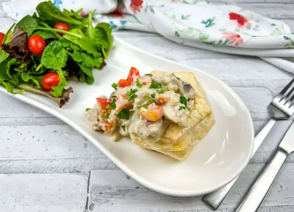 A white plate with a salad and a pastry on it.