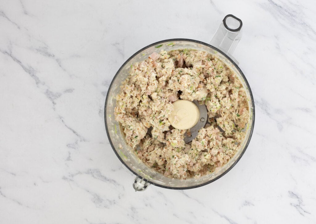 Cream cheese mixed into ham salad in food processor bowl.