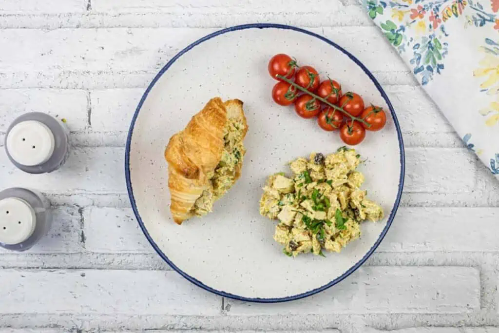 A plate with a croissant, Coronation Chicken Salad, and tomatoes.