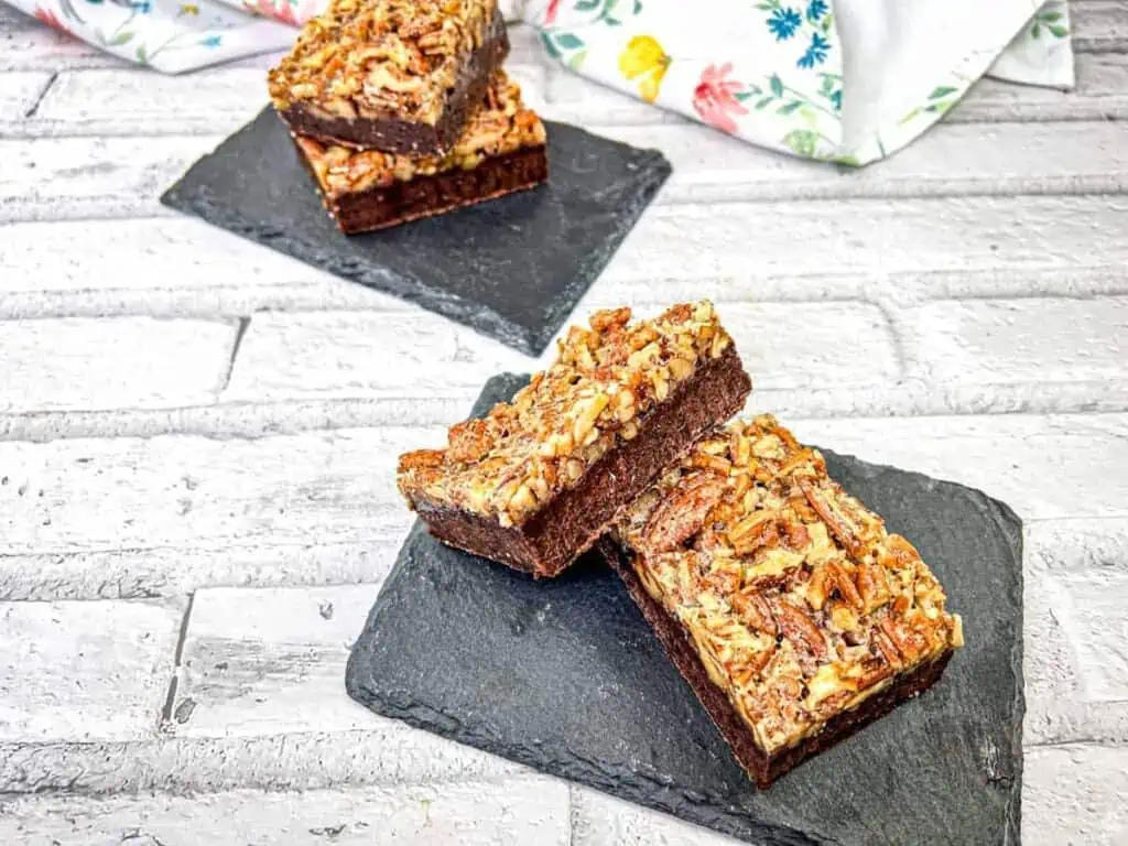 Three pieces of pecan pie brownies on slate coasters..