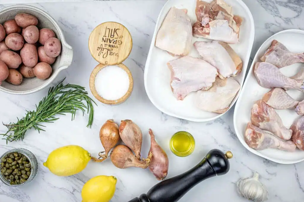 Chicken, potatoes, lemons and herbs on a marble table.