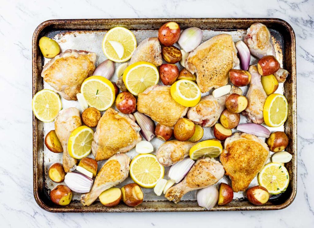 Chicken, potatoes and lemons on a baking sheet.