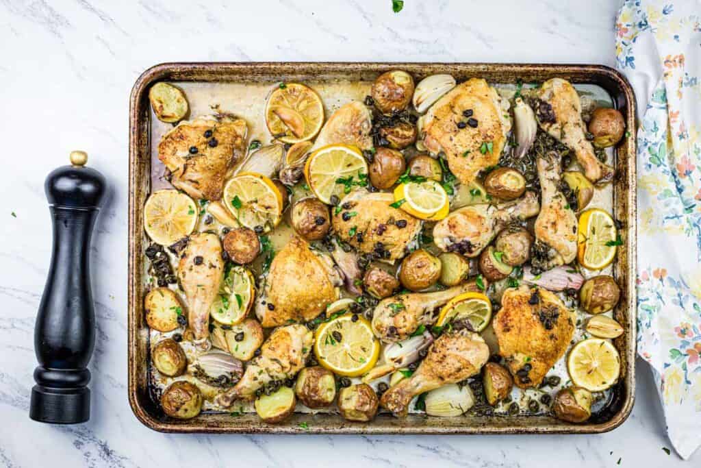 Chicken, potatoes and lemons on a baking sheet.