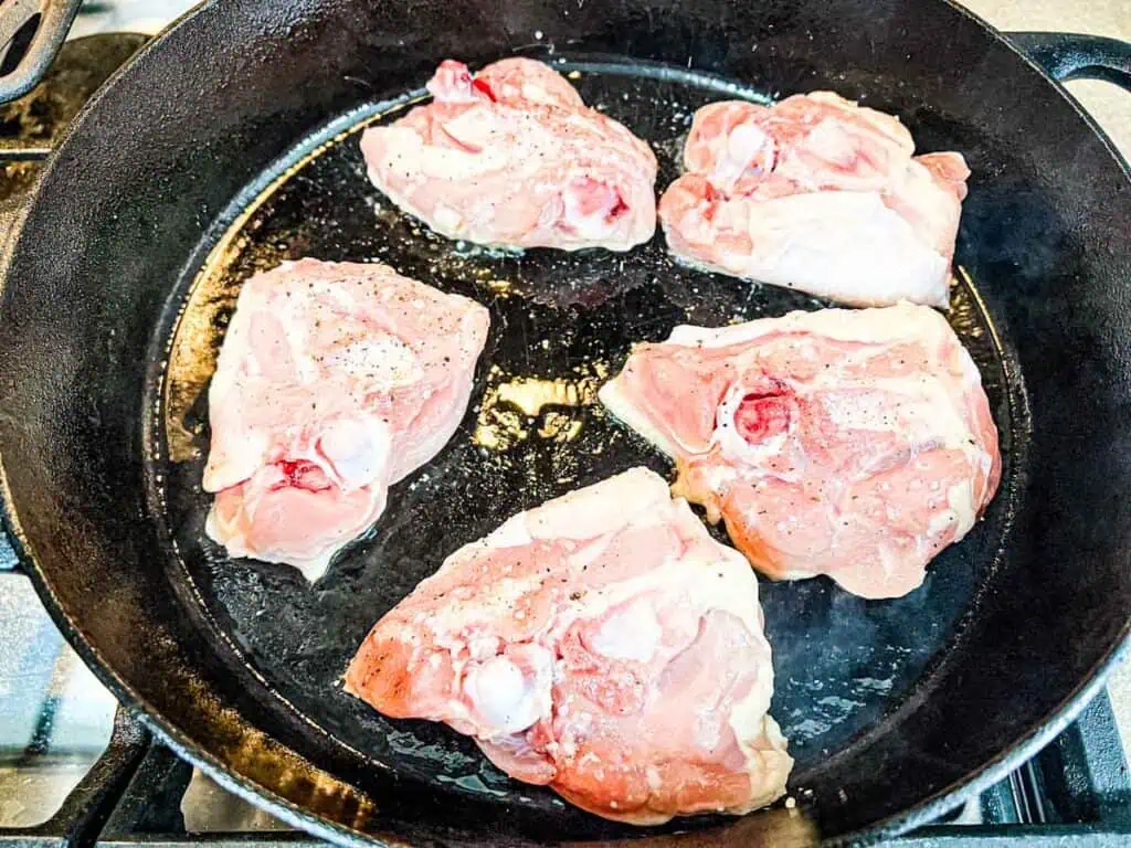 Pork chops in a frying pan on a stove.