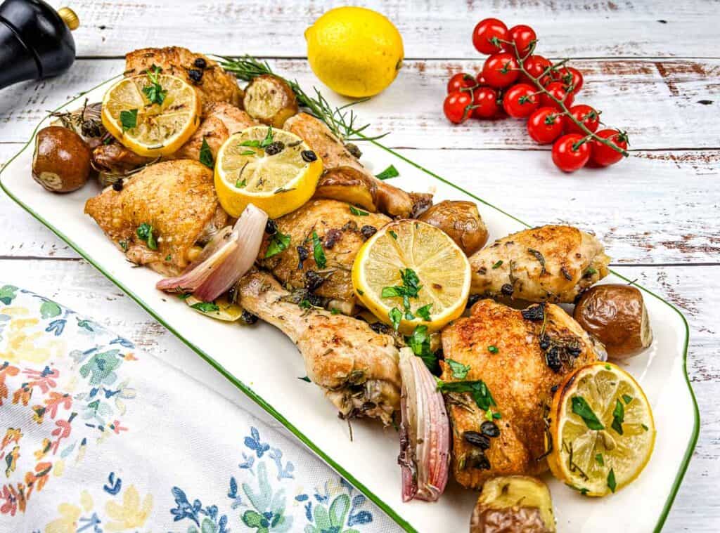 Roasted chicken with lemons and tomatoes on a white plate.