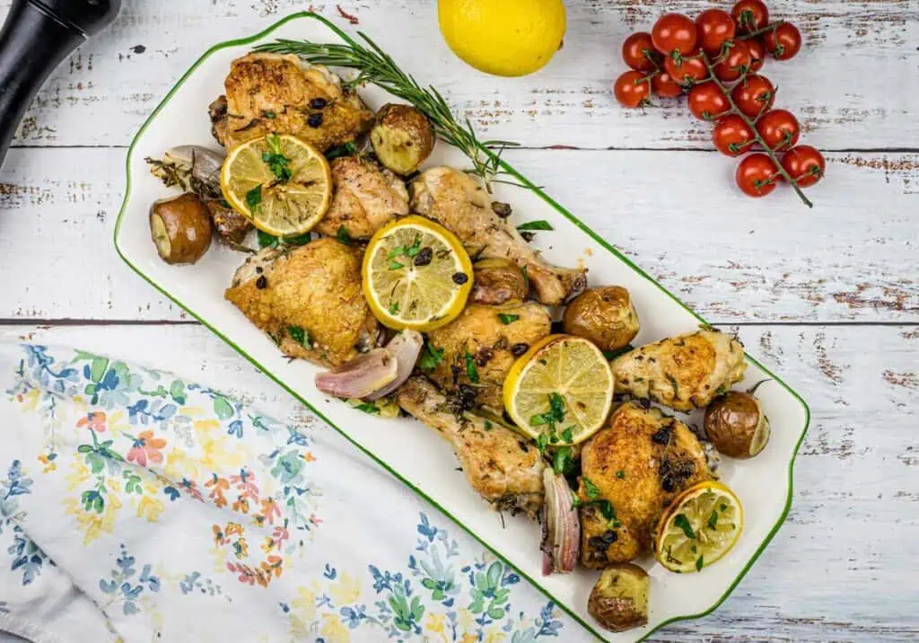 Roasted chicken with lemons and potatoes on a white plate.
