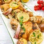 Roasted chicken with lemons and potatoes on a white plate.