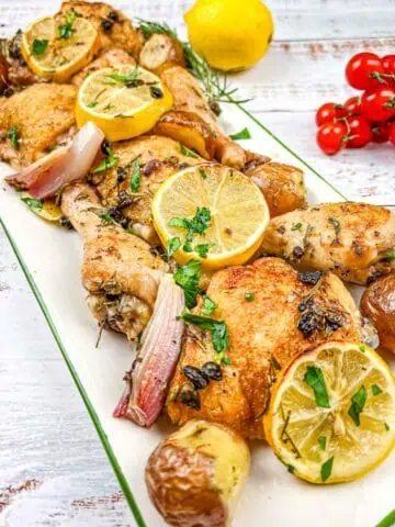 Roasted chicken with lemons and potatoes on a white plate.